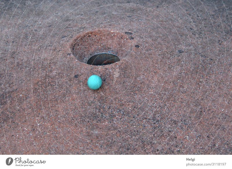 blue minigolf ball is just before the target at the edge of the hole Leisure and hobbies Playing Mini golf Ball Movement Authentic Small Round Brown Turquoise