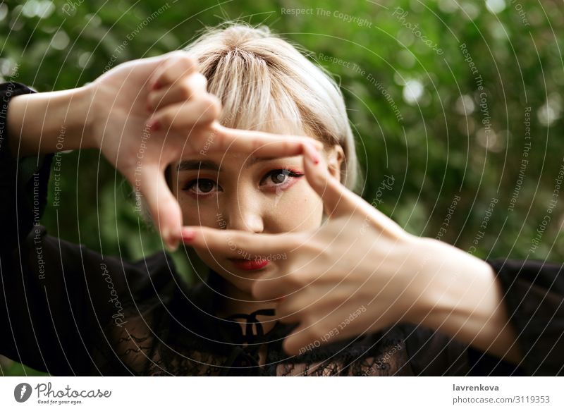 Closeup of young adult blond asian girl making frame gesture Eyes Park Close-up Photo shoot Frame Hand Lifestyle Face Blonde Asians 18 - 30 years Young woman