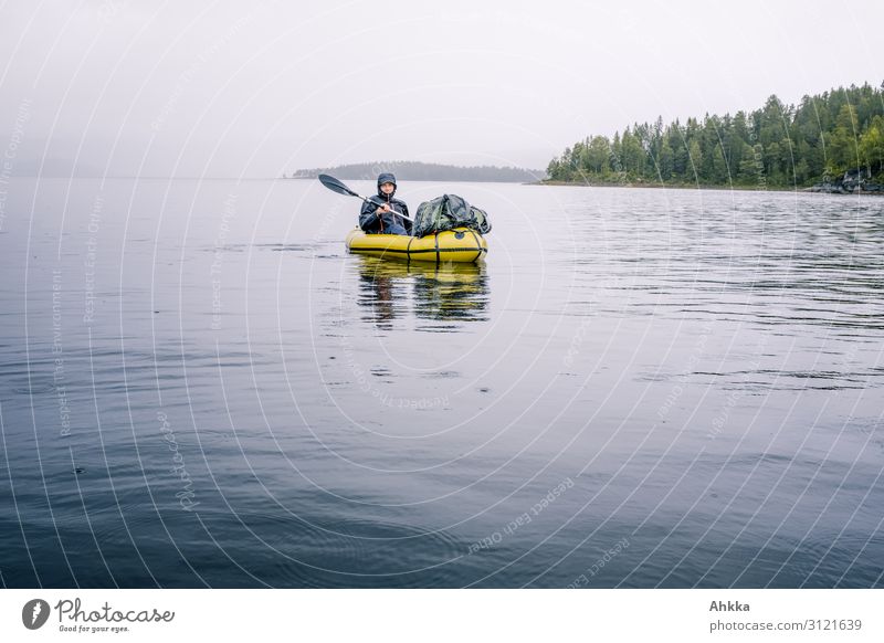 A young man rides a green kayak in the rain on a lake with shallow shores Rainy weather Wet boat Stay tuned hold on Boating trip Paddling Lake Water bank