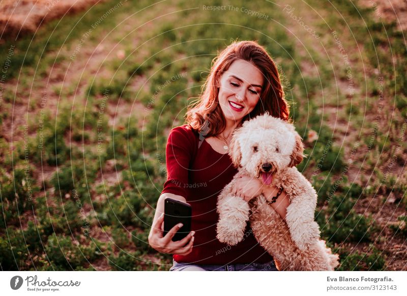 beautiful caucasian woman taking a selfie with her dog at sunset in countryside. Using mobile phone. Technology and lifestyle outdoors Youth (Young adults)