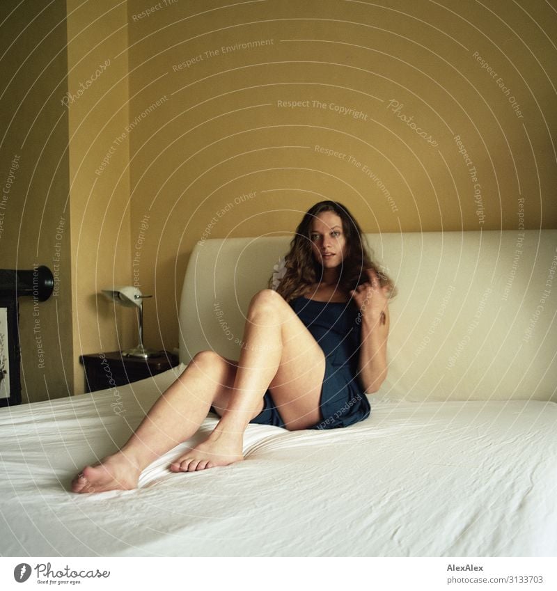 Portrait of a young woman on a white bed in front of a yellow wall Style already Life Living or residing Bed Young woman Youth (Young adults) Legs 18 - 30 years
