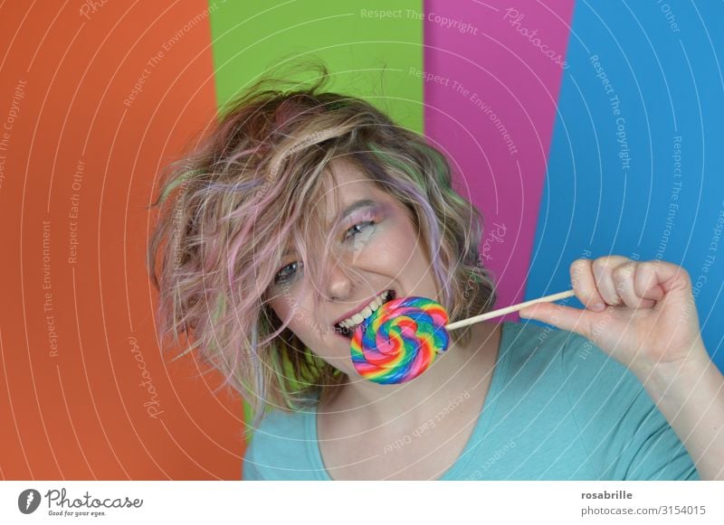 young blonde woman with coloured strands of hair biting into a giant coloured lollipop Candy Joy Happy Beautiful Hair and hairstyles Make-up Contentment