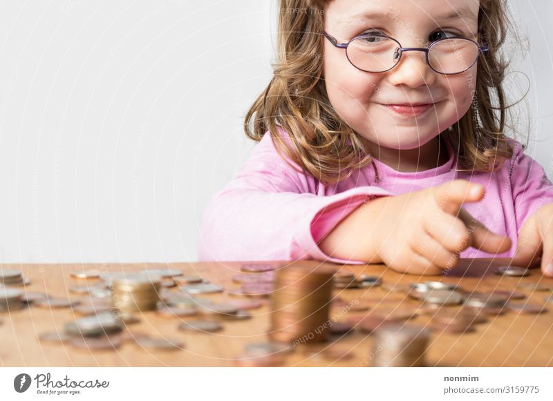 Smiling girl wearing glasses dressed in pink counting coins for savings. Focus on the face. Clean neutral background and copy space on the left. Money Save