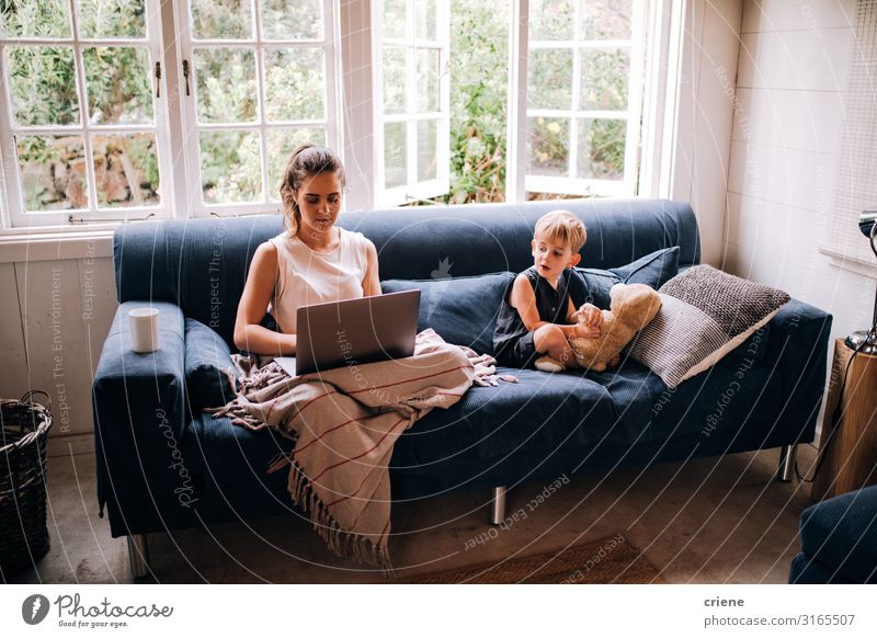 Mother working on laptop next to her son Lifestyle Happy Relaxation Leisure and hobbies Reading Sofa Child Work and employment Business Computer Notebook