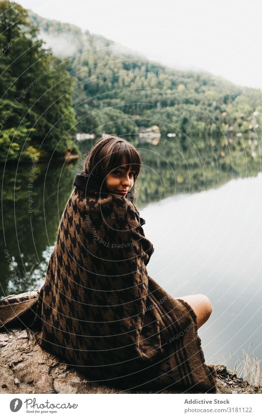 Woman sitting with blanket near lake and mountains Sit Blanket Lake Mountain Picturesque Water Coast Surface Amazing Vantage point Hill Stone Sky Clouds Rock