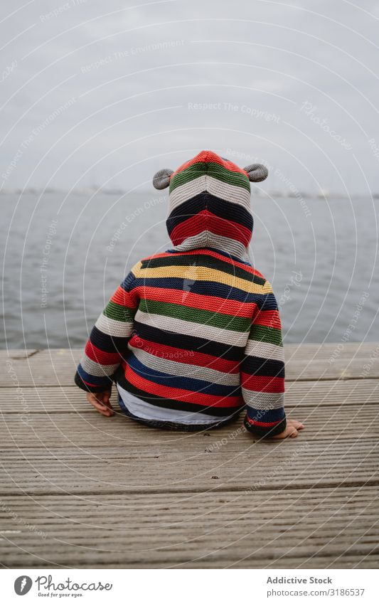 Anonymous kid sitting on pier Child Jetty Ocean Sit Baby Easygoing Lifestyle Leisure and hobbies Rest Relaxation Striped Jacket Car Hood marine Water Coast