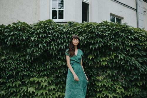 woman wearing an elegant green dress is standing in front of hedge adult attractive beautiful woman charming chic city classic clothing confident europe