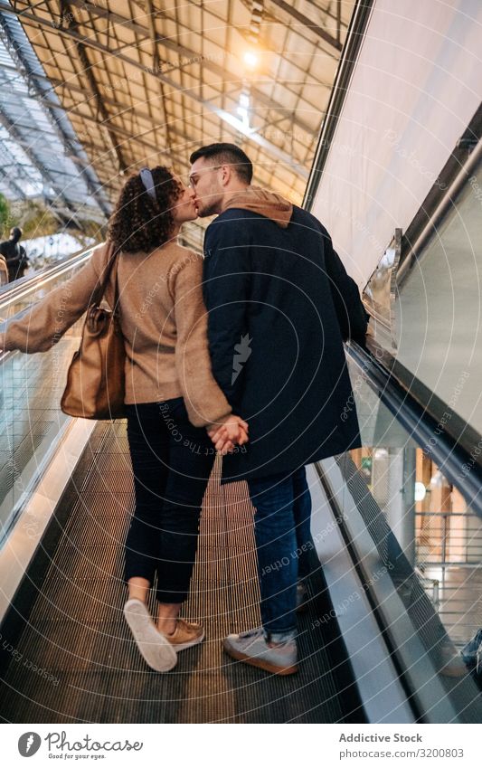 Young couple kissing riding travelator in mall Couple Moving pavement Mall holding hands Date Youth (Young adults) Together Illumination Lifestyle
