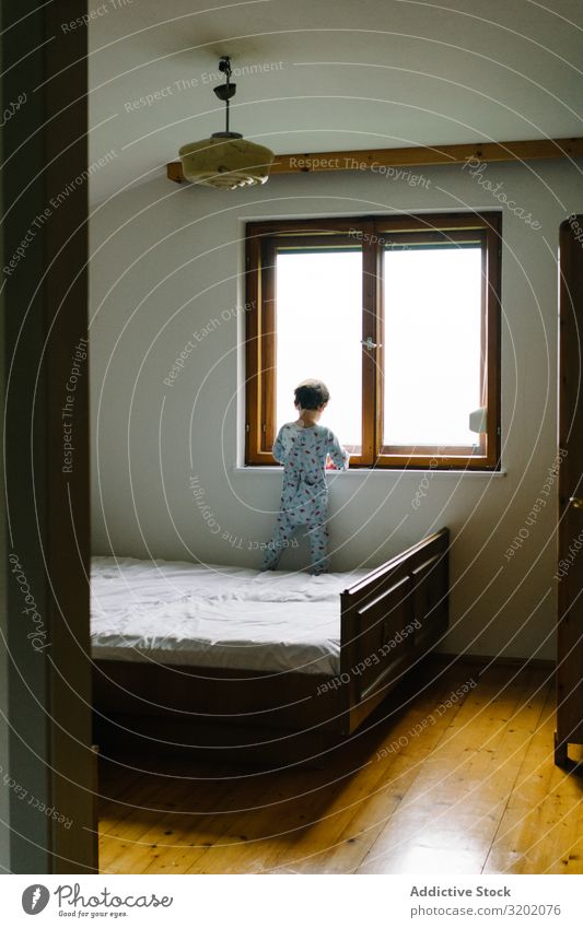 Child in pajamas standing on bed and looking out window Window Bedroom Leisure and hobbies Cheerful Lifestyle enjoyment Observe Delightful Beautiful Freedom