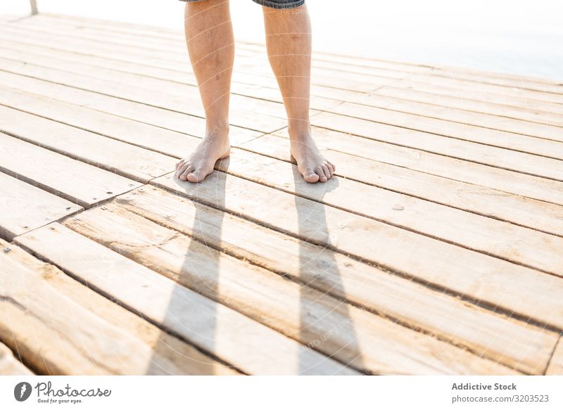 Legs of adult standing on wooden pier in sunlight Man Stand Jetty Feet crop view Summer Contentment body part Nature Leisure and hobbies Adults Sunbathing Water