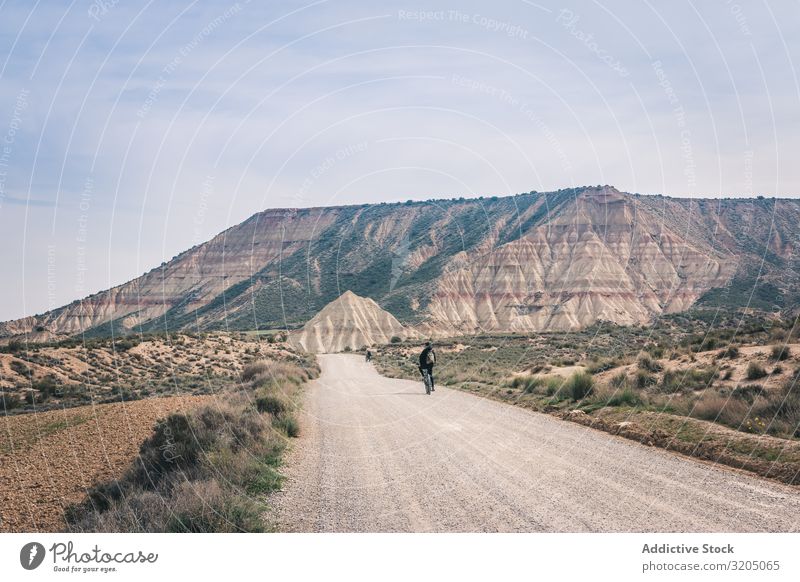 Man riding bicycles on road in desert hills Bicycle Street Desert Hill Landscape Sand Stone Plant Trip Dry Nature Sky Vacation & Travel Hot Destination