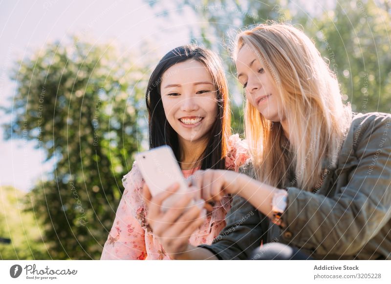 Female friends using smartphone in park Friendship PDA Park Indicate Smiling Mixed race ethnicity Woman Youth (Young adults) Share Together Lifestyle