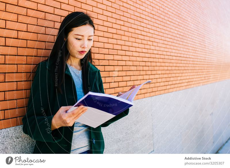 Asian student reading textbook near brick wall Student Reading Manual Lean Wall (building) Brick asian Woman Academic studies Youth (Young adults) Notebook