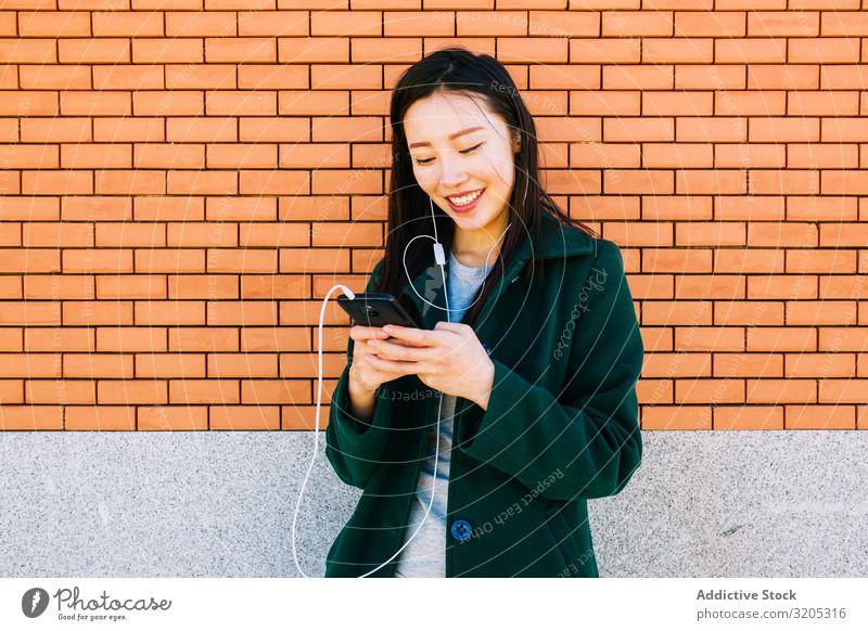 Asian female listening to music near brick wall Woman Listening Music PDA using Wall (building) Lean Brick Street City asian Ethnic Lifestyle