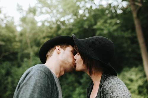 young heterosexual couple wearing hats kissing each other affection bonding casual caucasian charming cute date dating day daytime emotional enjoy enjoyment