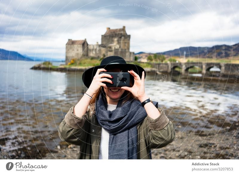 Smiling traveling woman photographing with phone scotland taking photo smartphone nature aged castle old cost photography lake trendy using tourism carefree