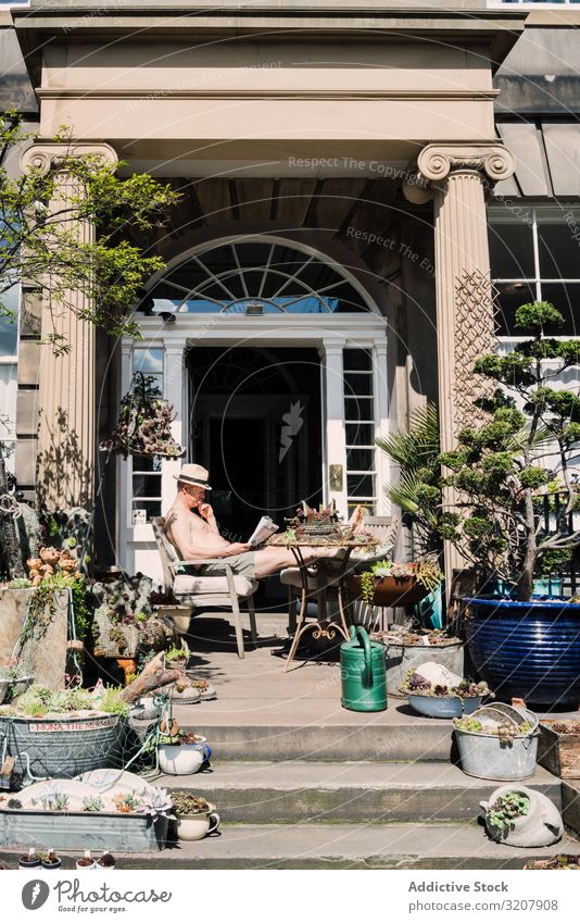 Man on porch with decorative plants in sunlight scotland lifestyle newspaper man leisure reading design gardening decoration residential nature house morning