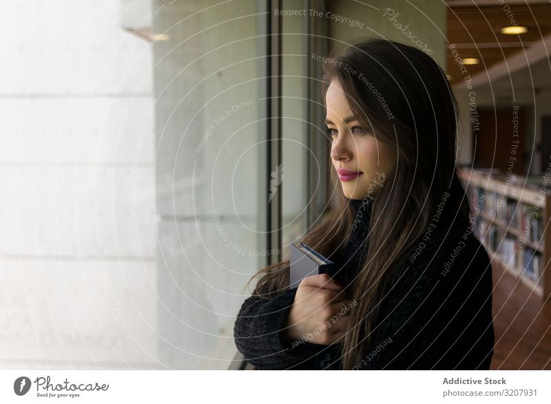 Pretty woman with book looking out window attractive smart clever beautiful brunette young female cute beauty pretty cheerful casual student elegant confident