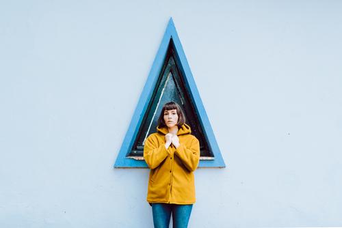 Cheerful female near triangle window woman smile building wall gray young happy standing coat casual jacket warm cheerful joy exterior geometric shape glad lady