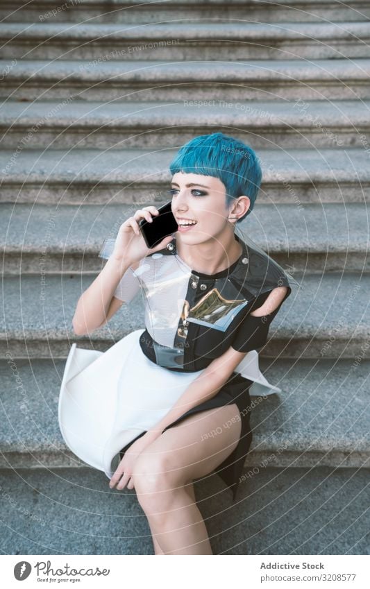 Young futuristic woman using smartphone on steps alternative dress trendy street urban listening subculture smiling fashion blue hair generation informal