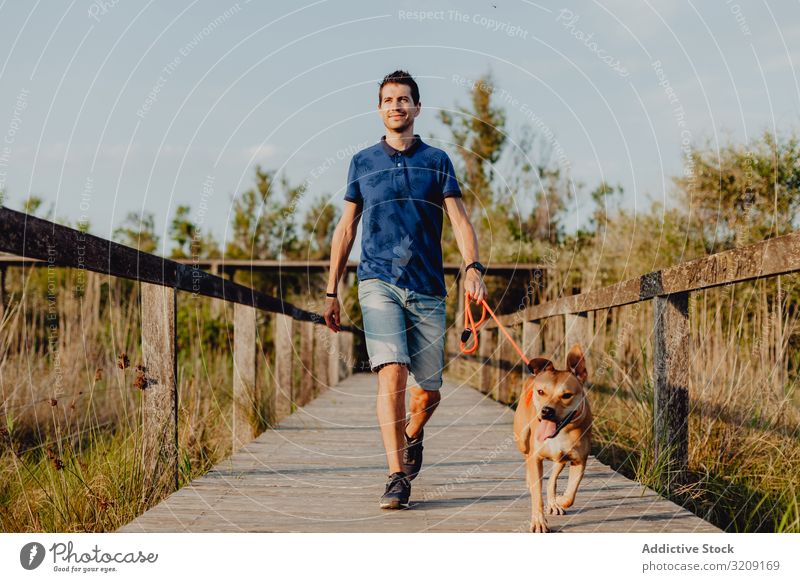 Happy adult man walking with dog along countryside run happy casual cheerful leash brown rural wooden tree greenery daylight pet together lifestyle smile fun
