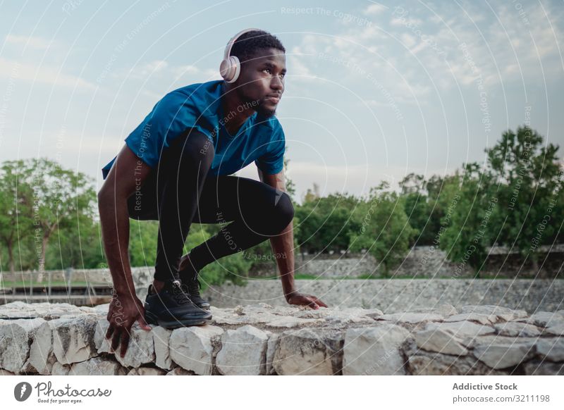 Black focused sportsman in squat waiting crouch start headphones healthy determined runner freedom muscular training strong technology ethnic fitness music