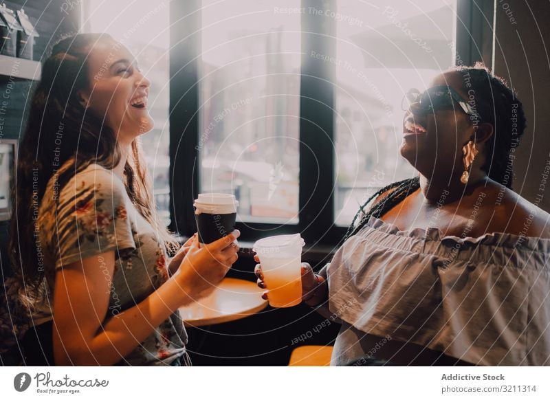 Multiethnic modern women relaxing at coffee shop laughing drink trendy sunset friend multiethnic multiracial african american black window cafe cup table