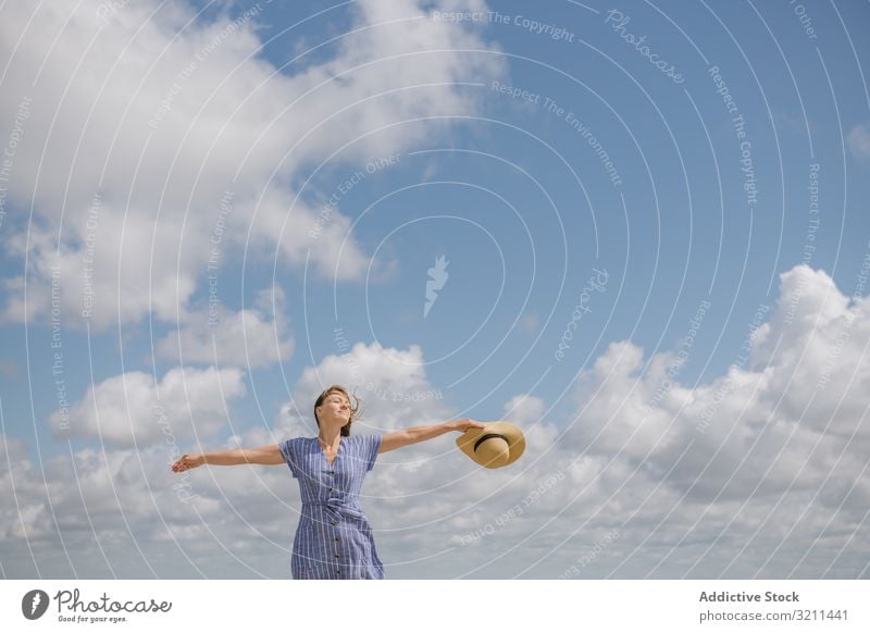 Happy young woman enjoying breeze happy carefree freedom wind sundress summer walk flying hair calm straw hat positive smiling cloud sky blue peaceful content