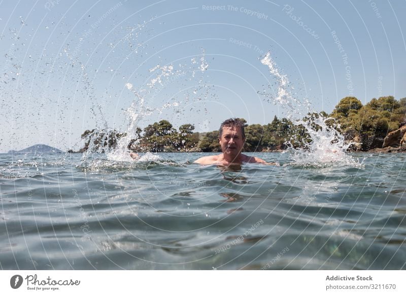 Active senior man swimming and splashing in water elderly retired travel mustache vacation halkidiki greece athlete sunlight sea ocean marine nautical summer