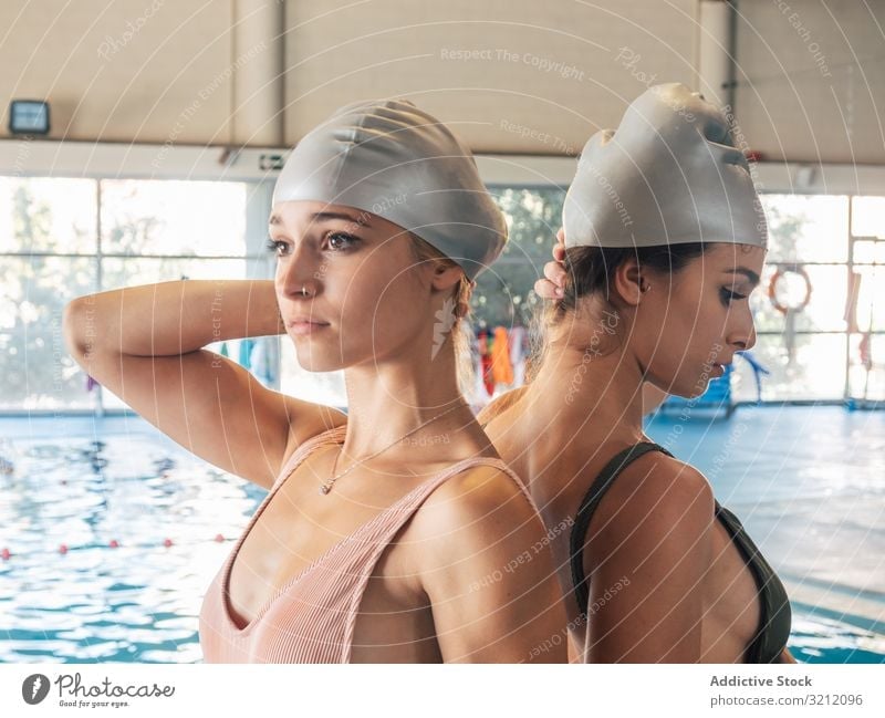Slim ladies wearing swimming caps in pool women young team water gym female friend facility back to back protection partner together leisure lifestyle swimwear