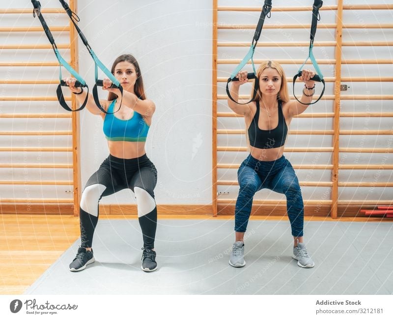 Strong ladies squatting with ropes sportswomen training suspension fitness athlete exercise trx wellbeing determination equipment sportswear gym workout