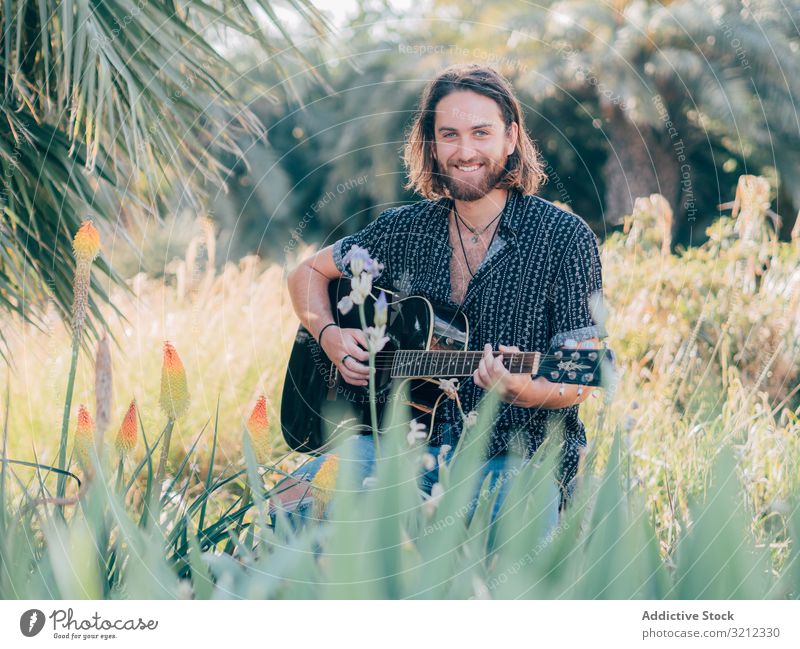Hipster man in meadow with guitar hipster musician sitting jungle playing adventure trip summer lifestyle pensive male acoustic young entertainment leisure