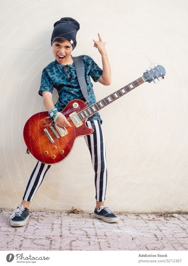 Energetic kid gesturing rock holding guitar boy playing rockstar colorful childhood fashion sign gesture artist musician festive laugh little contemporary funny