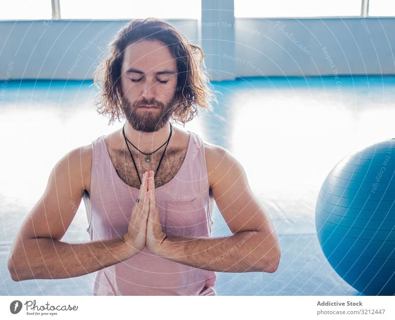 Male meditating in spacious room man meditate gym lotus relax yoga vitality zen harmony fitness exercise asana sport legs crossed young calm peace male bearded