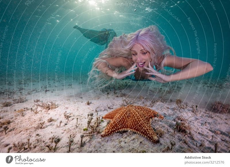 Redhead fairytale female mermaid swimming beside starfish underwater fishtail curious blue sea deep readhed beautiful daylight woman shiny seashell crown