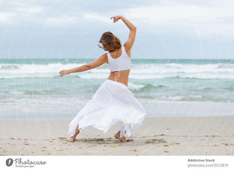 Anonymous woman dancing near sea sand shore freedom concept nature waves weather female movement posture white outfit coast beach ocean water carefree lady