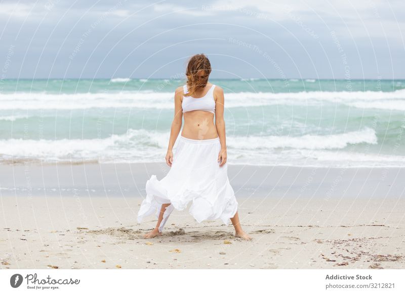 Beautiful woman dancing near sea sand shore freedom concept nature waves weather female movement posture white outfit coast beach ocean water carefree lady