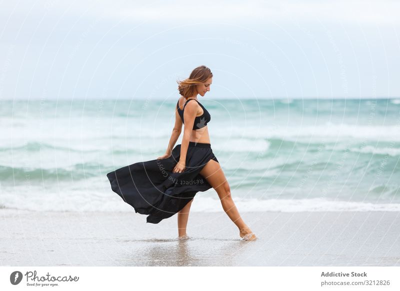 Beautiful woman dancing near sea sand shore freedom concept nature waves weather female movement posture black outfit coast beach ocean water carefree lady