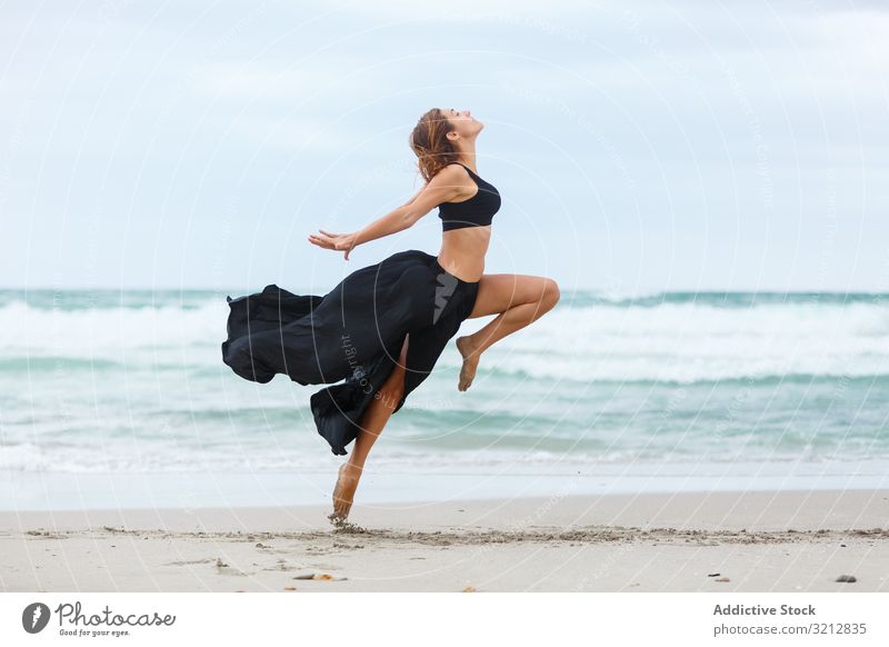 Beautiful woman dancing near sea sand shore freedom concept nature waves weather female movement posture black outfit coast beach ocean water carefree lady