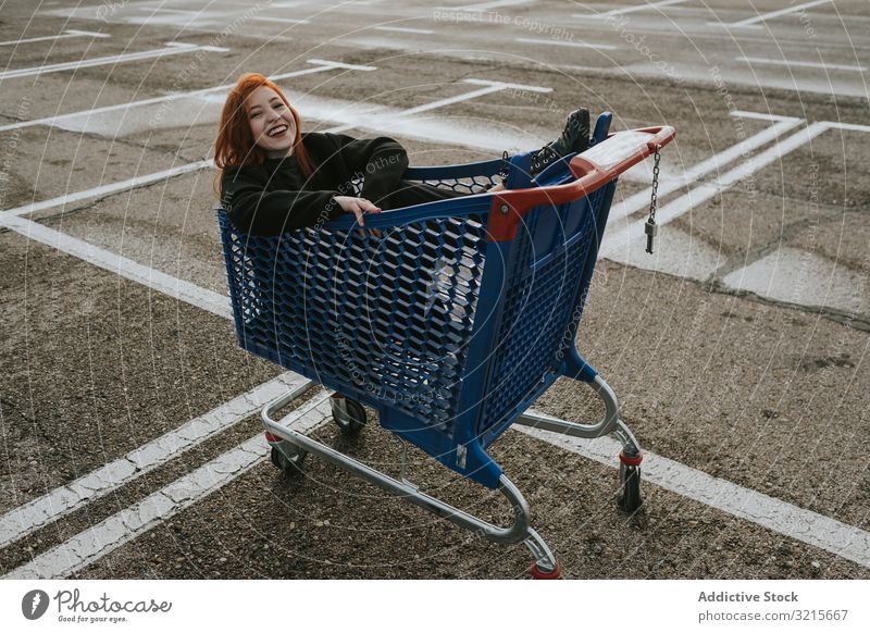 Smiling woman sitting in shopping trolley in parking lot attractive young beautiful having fun casual smiling smart modern shopping cart joy redhead female