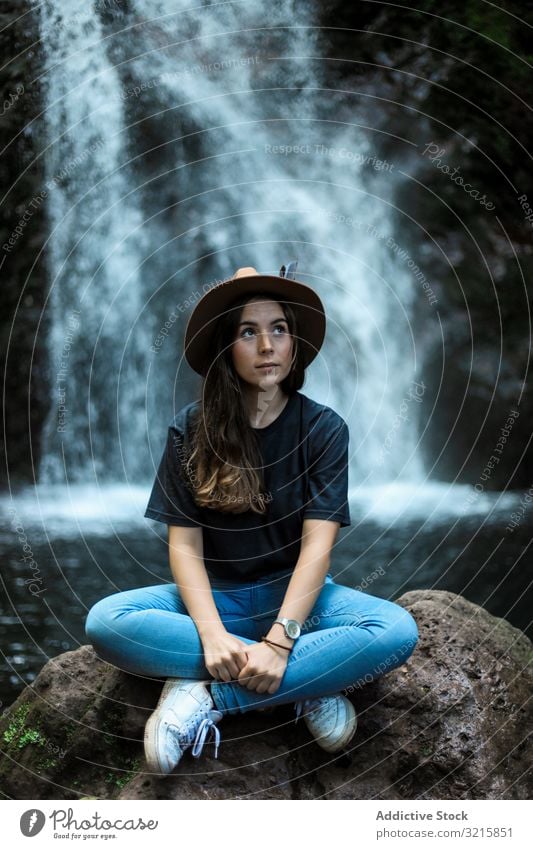 Smiling woman sitting near waterfall copy space stone casual wanderlust flow rock stylish lady stream smiling friendly female rest looking at camera cheerful