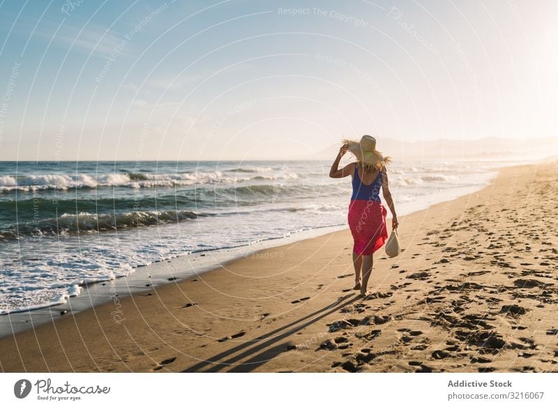 Woman holding hat and walking along seaside woman beach sandy swimwear pareo water ocean summer enjoying leisure athletic sporty body happy slim wavy sunny