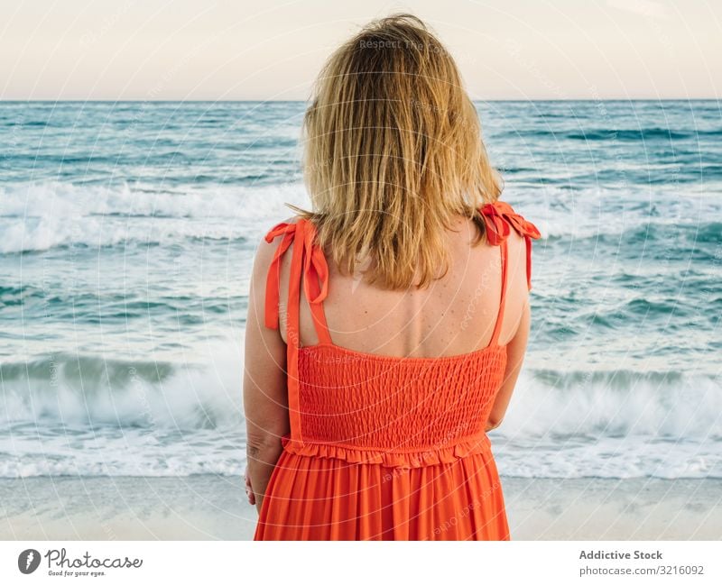 Woman in red dress looking along at seaside woman beach sandy water waves thoughtful enjoying summer relaxing leisure seascape female lifestyle vacation