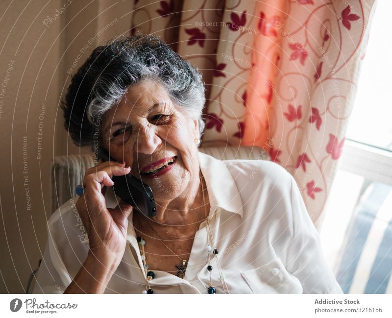 Cheerful elderly woman talking on cell phone at home aged mobile phone grandmother experience wisdom modern conversation attention grandparent generation senior