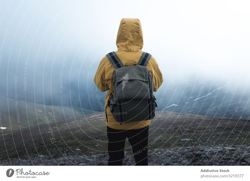 Anonymous traveler on hill on misty day man hillside fog nature weather backpack stand countryside hiking male trekking trip journey tourism adventure slope