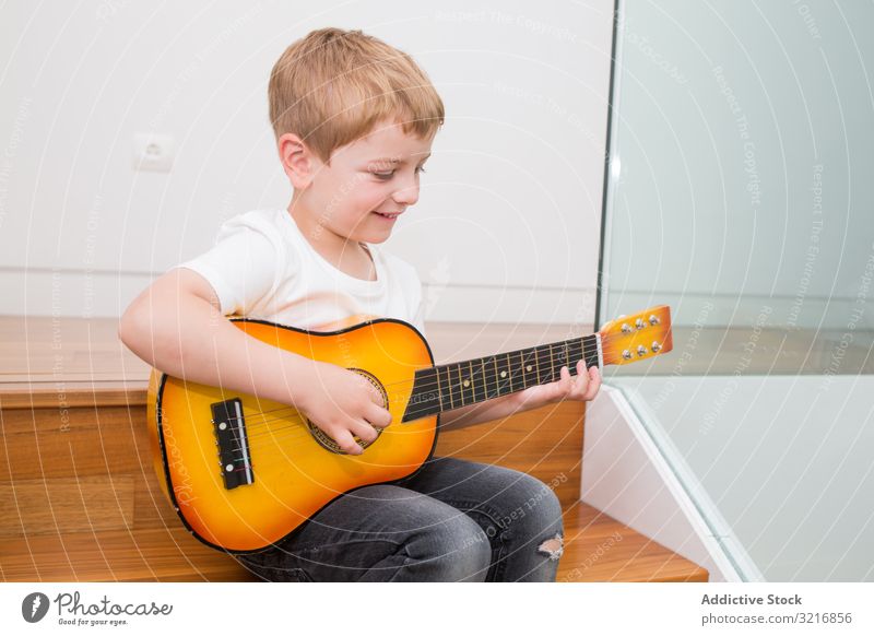 Young blonde boy playing toy guitar music instrument kid hobby musician talented child little male casual cute adorable concentrated sitting practicing white
