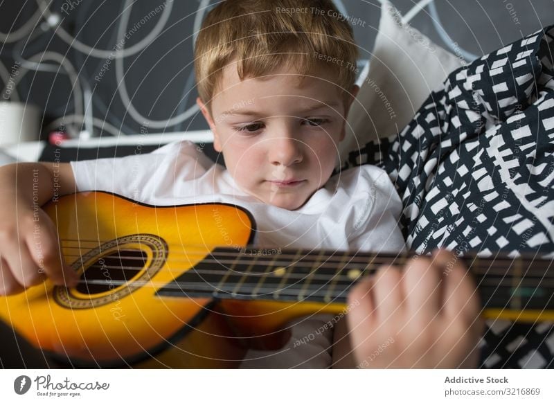 Young blonde boy playing toy guitar music instrument kid hobby musician talented child little male person casual cute adorable lying relaxing practicing white