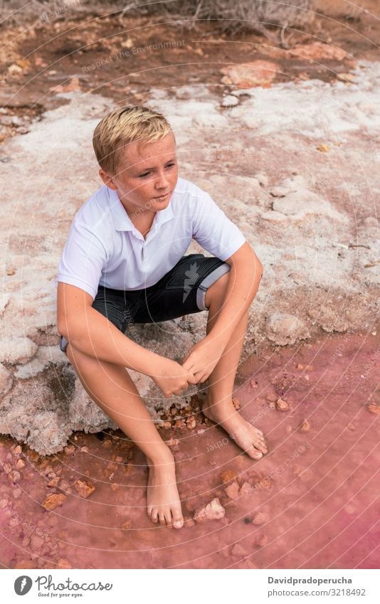 cute teenager blonde boy wearing summer clothes sitting on shore of an amazing pink lake young romantic freckles happy alone sea colorful adolescent nature