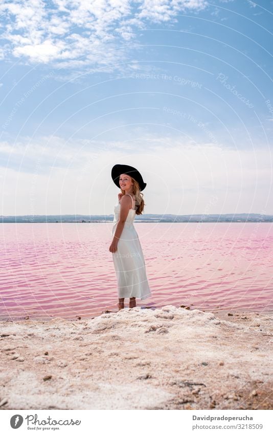 Back view of cute teenager woman wearing white dress walking on a amazing pink lake young saline romantic tourism summer happy alone sea colorful nature water