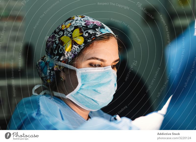 Concentrated female surgeon at work woman doctor surgery hospital operation medicine profession concentration young serious attentive surgical gown blue cap